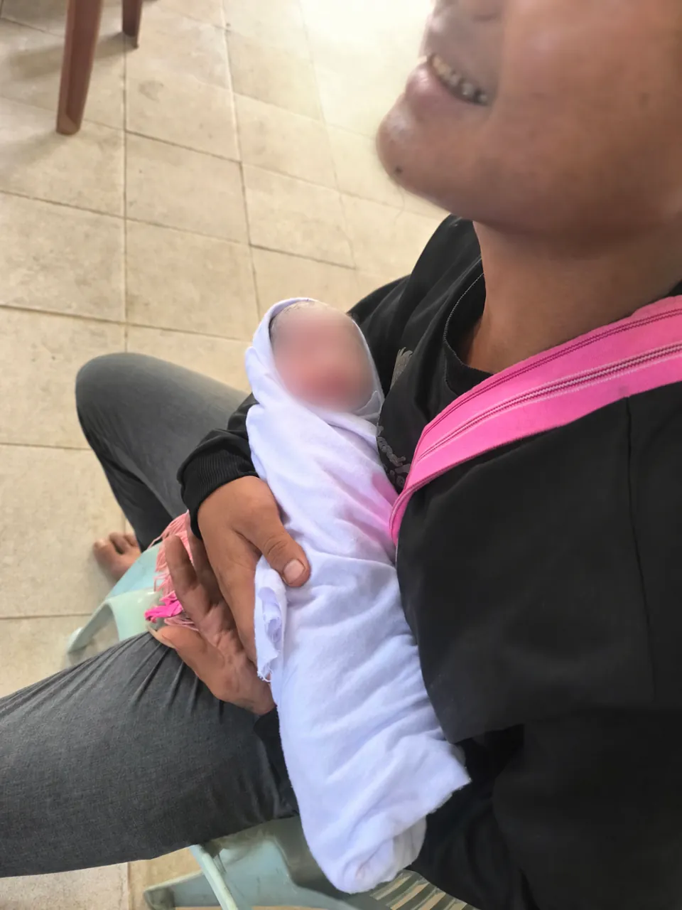 An adult holding a swaddled infant whose face is blurred for privacy.