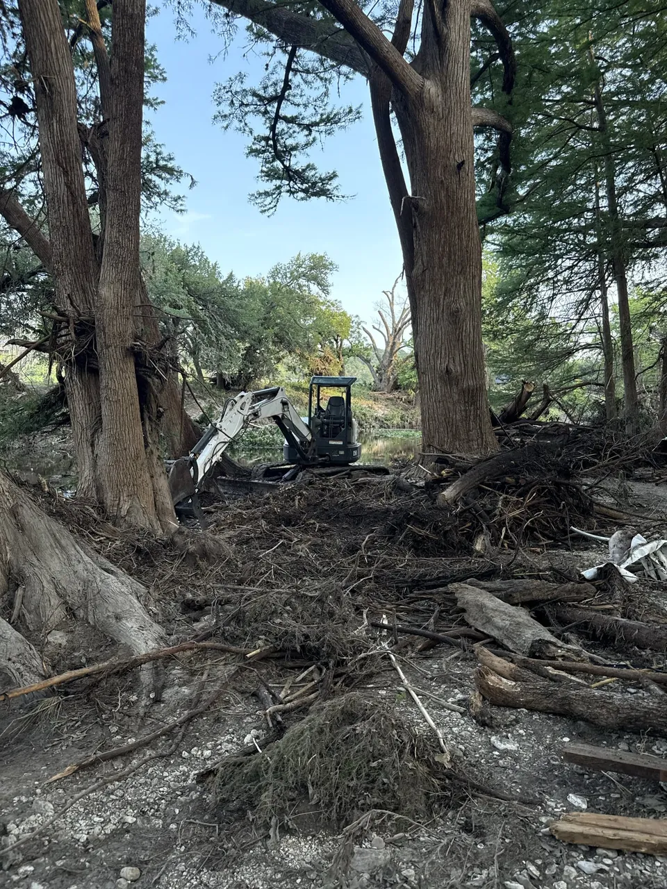 An excavator among trees and flood debris.